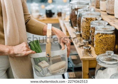 Close up shot of woman carrying shopping basket and shopping groceries zero waste shop with glass jars on shelves.. Royalty-Free Stock Photo #2274362513