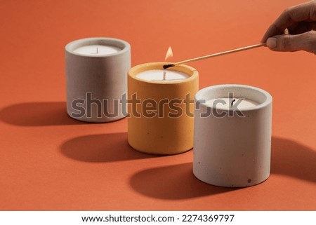 A hand lights a candle with a match stick. Aromatic soy candles in gray concrete jar. Poster banner for candle shop, beauty, spa