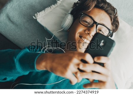 Cheerful young boy using phone app to listen music with headphones. Modern people chatting and dating online with cellphone device. Above view of student enjoying surfing net internet activity leisure Royalty-Free Stock Photo #2274374919