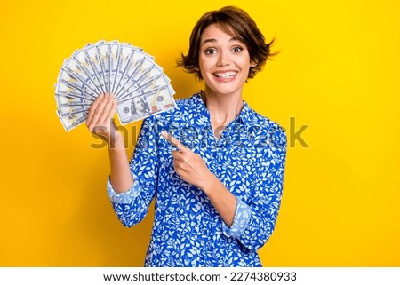 Photo of adorable excited lady wear print shirt pointing finger money fan isolated yellow color background