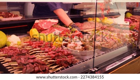 Mens hands picking chicken barbecue on skewers to be weighted. Window shop with different meat goods in butchers store. Royalty-Free Stock Photo #2274384155
