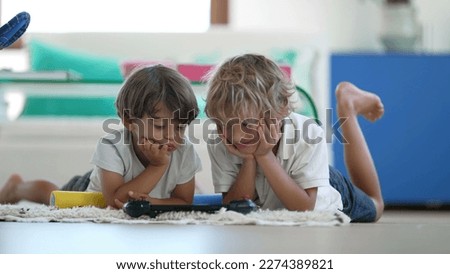 Candid of two young boys watching media on tablet screen lying on floor at living room floor at home. Children staring at technological device indoors