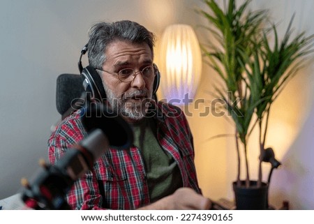 Man recording a podcast on his laptop computer with headphones and a microscope. Male podcaster making audio podcast from his home studio. Vlogger messaging his audience while making podcast at home 