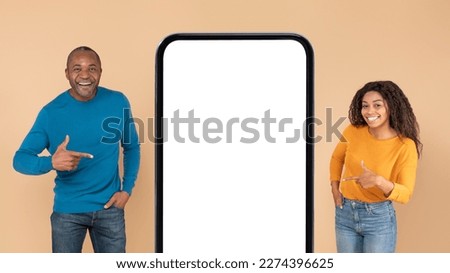 Excited african american couple pointing at large cellphone blank screen, showing place for your design, standing on beige background, mockup, panorama