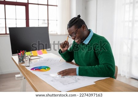 Cheerful African American Architect Guy Making Technical Drawing For A New Project Working Sitting At Desk With Big Computer In Office. Modern Architecture And Engineering Concept. Side View