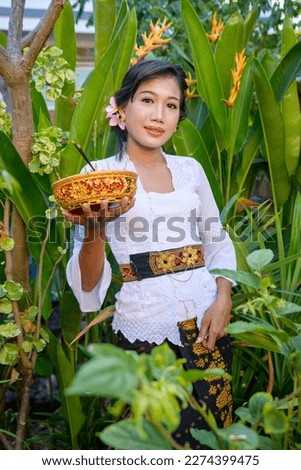Bali young woman with beautiful face and attractive full lips wearing white shirt and brown sarong in garden and dancing pose.