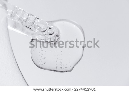 Close up of gel or serum glass pipette with transparent drops on white background. Cosmetics or medical concept. Minimalism style. Free space for text.