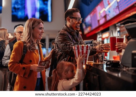 A young joyful Caucasian family is in the movie theater buying drinks, tickets and popcorn at the bar. Royalty-Free Stock Photo #2274424023
