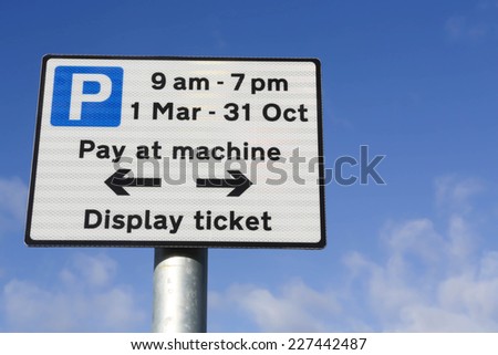 Pay at machine car park sign when parking between 9am and 7pm, March to October against a partly cloudy sky.