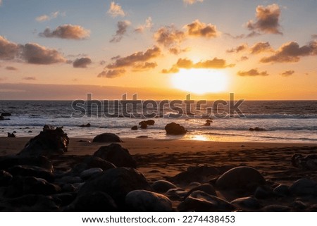 Scenic view during sunset on the volcanic sand beach Playa del Ingles in Valle Gran Rey, La Gomera, Canary Islands, Spain, Europe. Sun beam reflection on water surface. Stones in the foreground Royalty-Free Stock Photo #2274438453