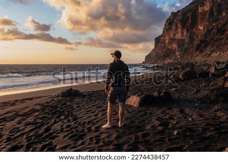 Woman in dress walking barefoot on volcanic sand beach Playa del Ingles during sunset in Valle Gran Rey on La Gomera, Canary Islands, Spain, Europe. Calm atmosphere seaside. Massive cliffs La Mercia Royalty-Free Stock Photo #2274438457