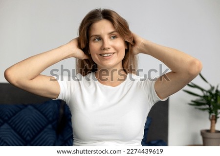 Portrait of beautiful woman looking away with happy smile and touching her hair. Attractive female  with long hair enjoying quality of her hair at home. Beauty concept