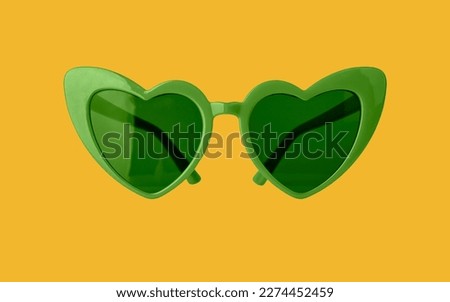 Heart-shaped green funky sun glasses on yellow background. Funny sunglasses for St Patricks day.