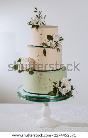 Three-tier pink and turquoise wedding cake decorated with cream flowers and elements of gold, on a white background