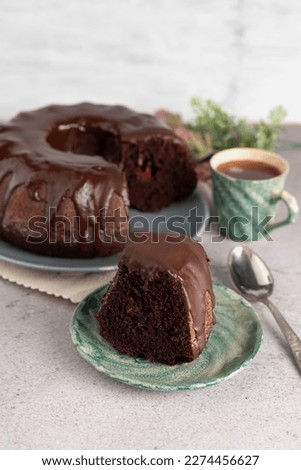 Blurred image of a slice of cake and a Bundt chocolate cake in the background, a cup of coffee on a light table. The concept of tea drinking.