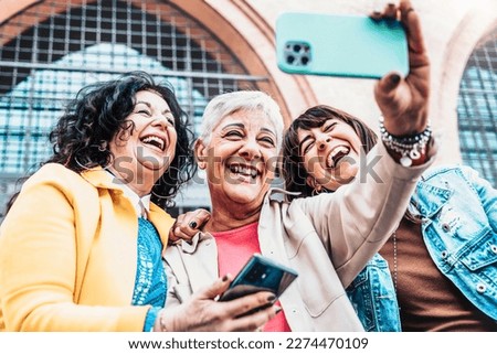Three cheerful women chilling outside taking group selfie and smiling - Happy female senior friends enjoying the weekend together while sightseeing an italian city - Elderly people lifestyle concept