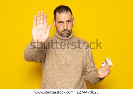 Hispanic man about 40 years old holding a euro bills isolated on yellow background standing with outstretched hand showing the stop sign, preventing you