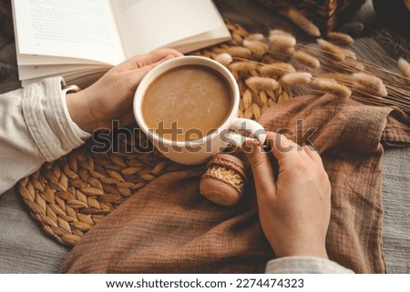 Cup of coffee in hands top view, macarons and open book, aesthetic photo.