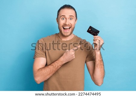 Photo of entrepreneur man wear t-shirt direct finger surprised demonstrate plastic credit card wireless nfc payment isolated on blue color background