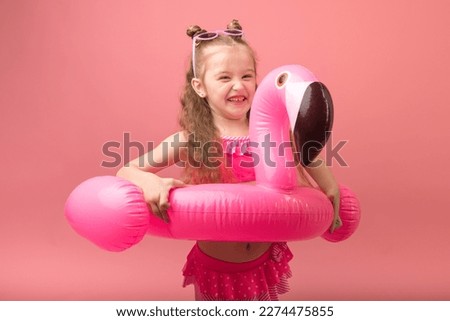Happy funny child girl in swimsuit with swimming ring flamingo on a colored pink background