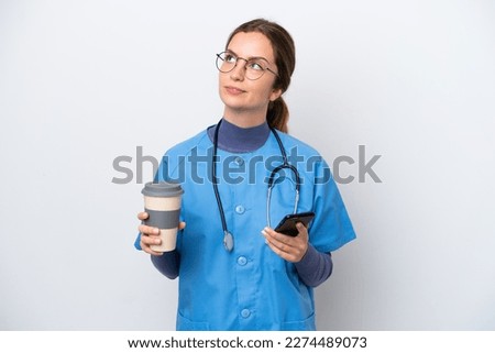 Young caucasian nurse woman isolated on white background holding coffee to take away and a mobile while thinking something