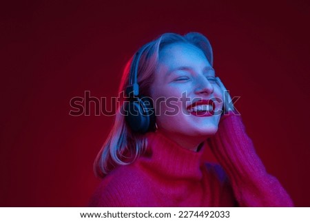 A joyful woman enjoying music and smiling with eyes closed while standing isolated on magenta background. Neon colored, viva magenta, color of the year.