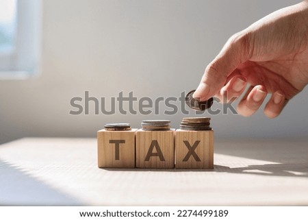 Hand put money coin to stack of coins above Tax word on wooden cubes.