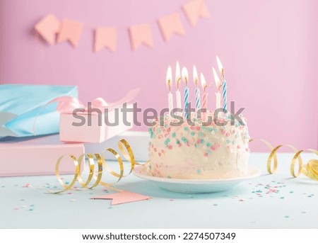 Festive cake with candles on the background of festive pink wall with gifts and flags in serpentine
