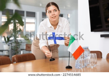 Young woman in business clothes puts flags of Finland and Italy on negotiating table in office