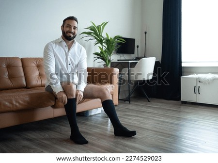 A man in a white shirt putting on black medical compression socks. Dressing up.