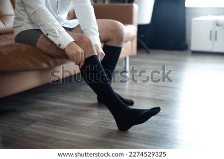A man in a white shirt putting on black medical compression socks. Dressing up. Royalty-Free Stock Photo #2274529325