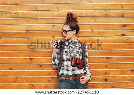 Outdoor lifestyle portrait of pretty funny hipster woman making photo. Retro photographer. Modern urban girl has fun with vintage photo camera, wooden background. Photo toned style Instagram filters.
