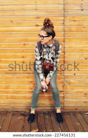 Outdoor lifestyle portrait of pretty funny hipster woman making photo. Retro photographer. Modern urban girl has fun with vintage photo camera, wooden background. Photo toned style Instagram filters.