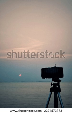modern technology smartphone placed on a tripod  Can be used to record stories, videos, pictures comfortably with the sunset view background of the sea and the natural sky at twilight time.