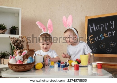 Two children with bunny ears funny painting Easter eggs at home. High quality photo