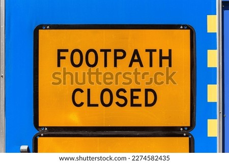 An reflective orange road sign with black lettering displaying FOOTPATH CLOSED