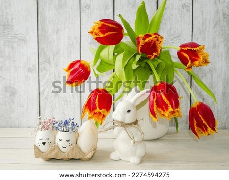 Easter decorative composition on a light wooden background in a vase spring flowers tulips, cute white rabbit, decorated Easter eggs.  Foreground, front view.  Concept holiday bright easter.