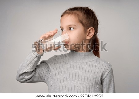 Cute little girl drinking water from glass on white background with copy space. 