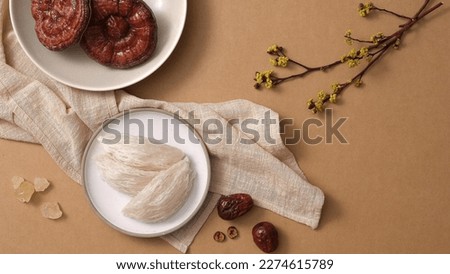 Salanganes nest raw on round dishes, red reishi mushroom, jujube on brown background. There are ingredients for distilling premium bird's nest. Top view, flat lay. Royalty-Free Stock Photo #2274615789