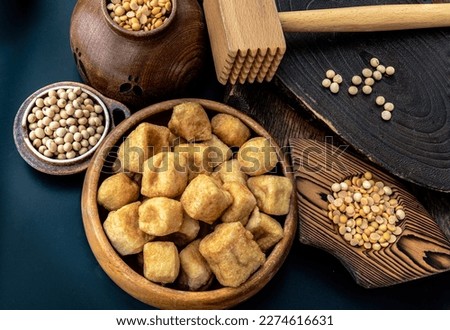 Brown fried tofu puffs or Deep Fried Tofu in wooden bowl and grains (soybeans) with dark background. Space for text. Royalty-Free Stock Photo #2274616631