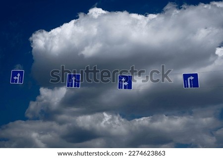 travelling pointer. Information sign, low angle view. Hanging blue traffic signs against bright blue cloudy sky background. white arrows.
