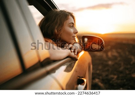 Happy woman outstretches her arms while sticking out the car window. Lifestyle, travel, tourism, nature, active life.