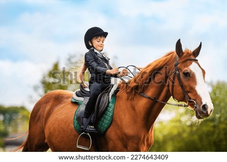 Small child in jockey outfit is riding horse on blue sky with clouds background. School of riding and equestrian sports. Royalty-Free Stock Photo #2274643409
