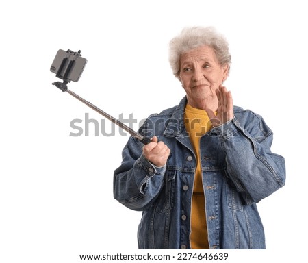 Senior woman with mobile phone taking selfie on white background