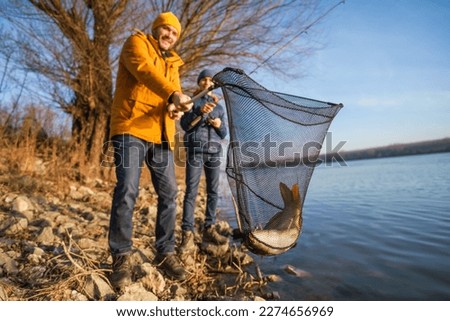 Father and son are fishing on sunny winter day. They caught a fish and are holding it in a landing net. Royalty-Free Stock Photo #2274656969