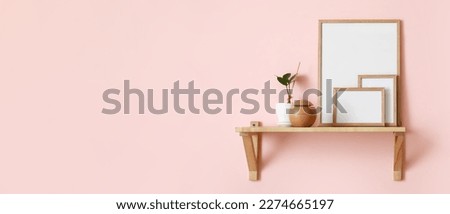 Blank photo frames, air freshener and houseplant on shelf hanging on light pink wall. Banner for design