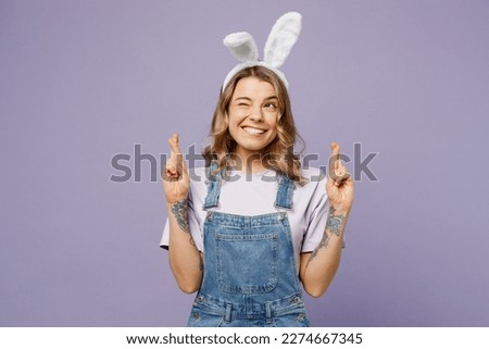 Young woman wearing casual clothes bunny rabbit ears waiting for special moment, keeping fingers crossed, making wish isolated on plain pastel light purple background. Lifestyle Happy Easter concept