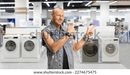 Bald man in a denim vest pointing at an appliance store