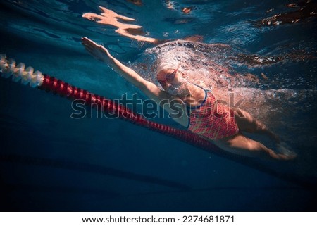 Dynamic shot of professional female swimmer training in swimming pool indoor. Developing speed. Underwater view. Concept of sport, endurance, competition, energy, healthy lifestyle Royalty-Free Stock Photo #2274681871