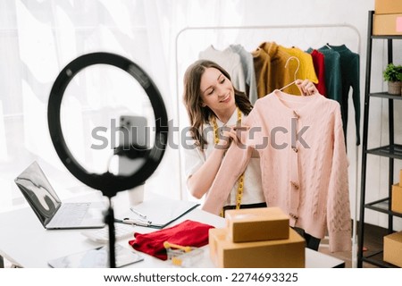 Fashion blogger concept, Young Asian women selling clothes on video streaming.Startup small business SME, using smartphone or tablet taking receive and checking at office

 Royalty-Free Stock Photo #2274693325